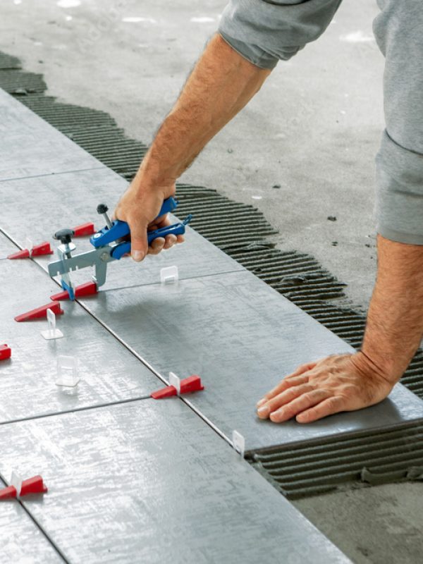 Ceramic Tiles. Tiler placing ceramic wall tile in position over adhesive with lash tile leveling system - Image